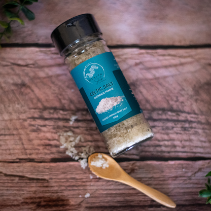 HealthStack Bottle of Celtic Salt on a wooden surface with a wooden spoon and salt crystals.